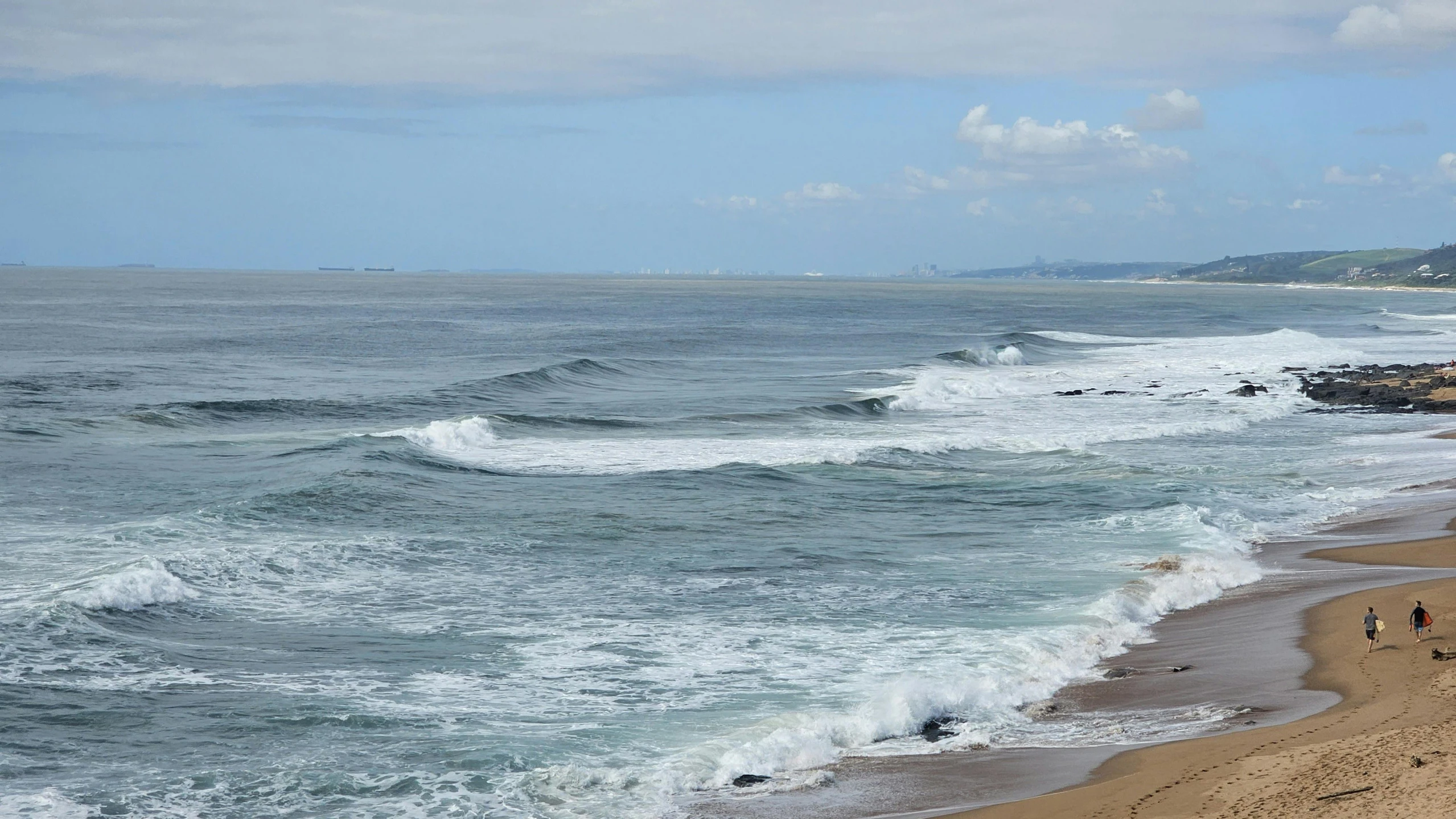 a few people walking on the beach along the ocean