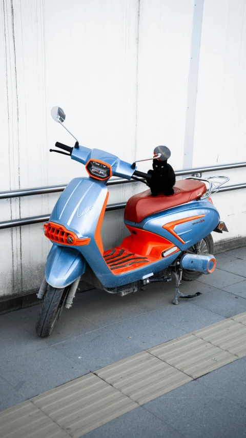 a man standing near an orange and blue motor scooter