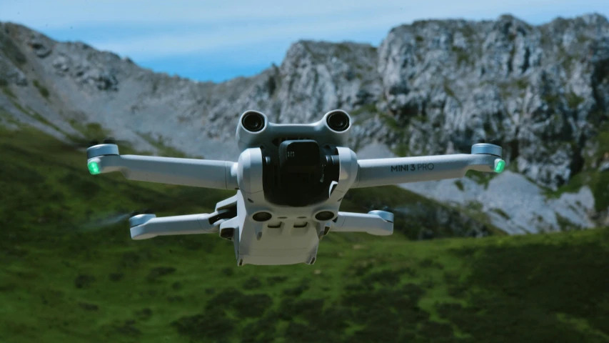 a flying gray and white small sized device in front of a mountain