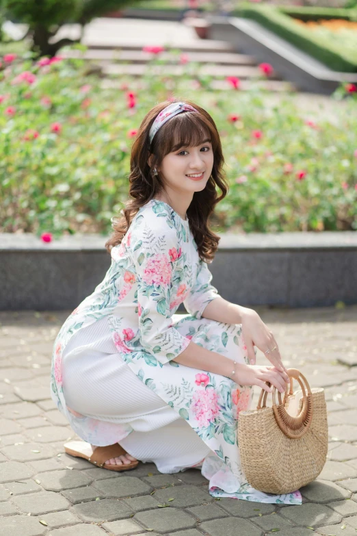 a woman in a floral print dress sits on the ground holding a bag