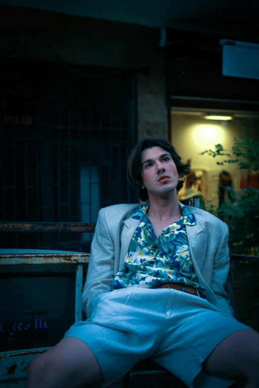 a man with a suit jacket and flower shirt sits on a chair