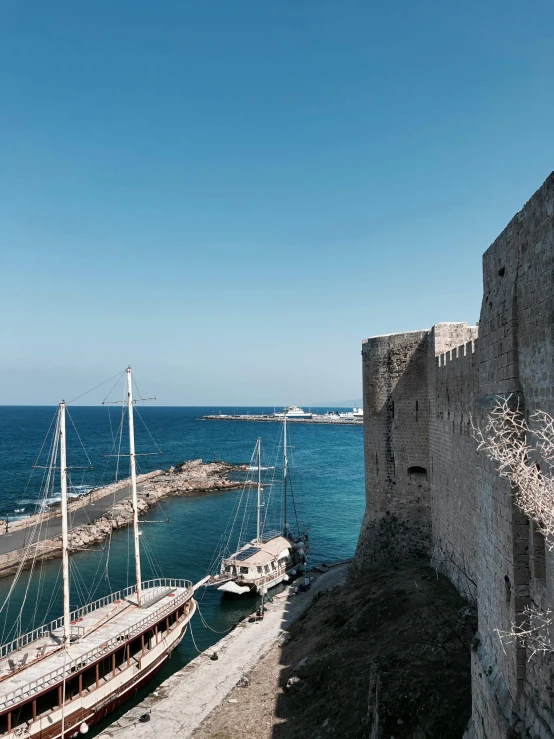 a sailboat floating beside a stone wall by the water