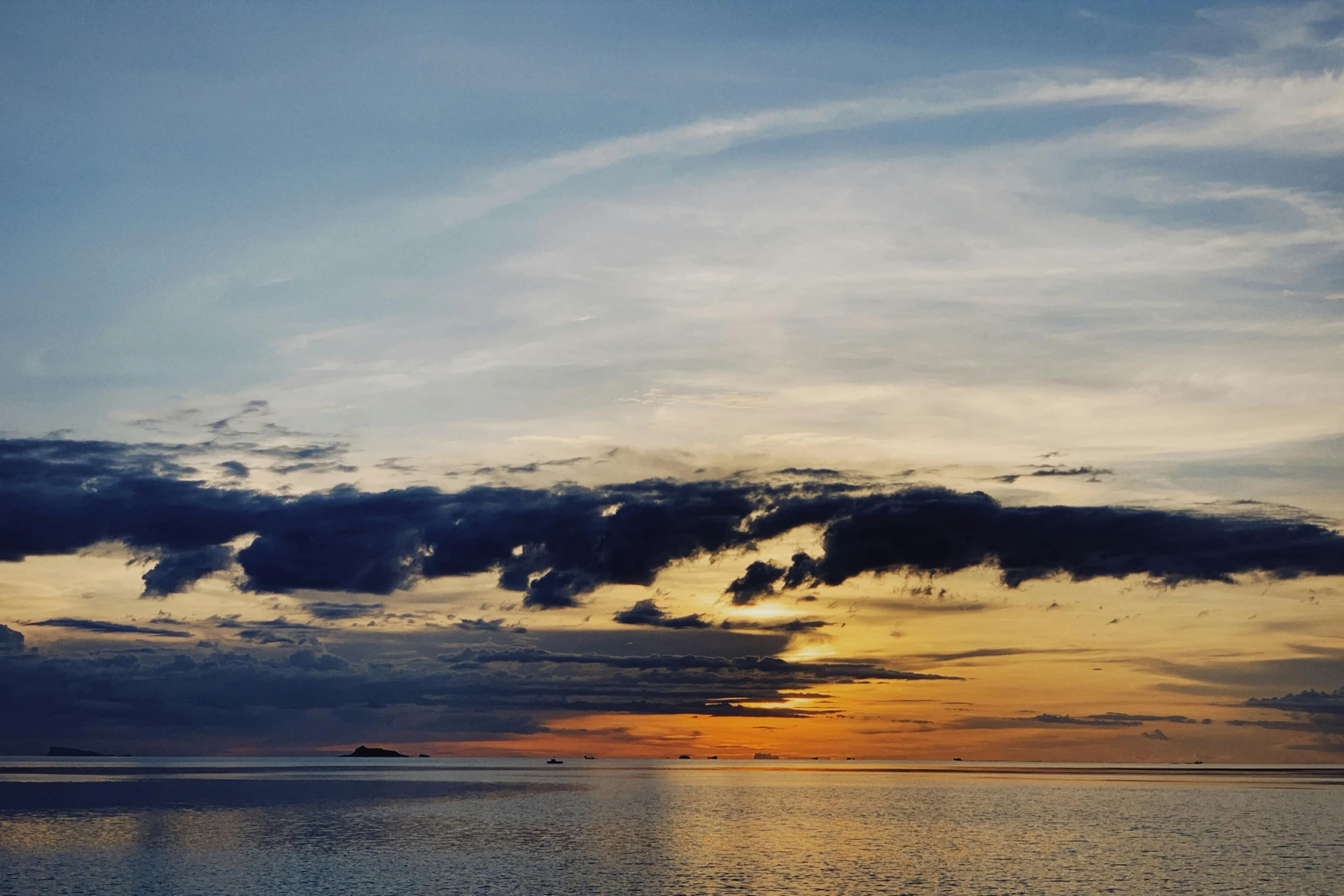 the sun is setting on the horizon as a small boat floats in the water