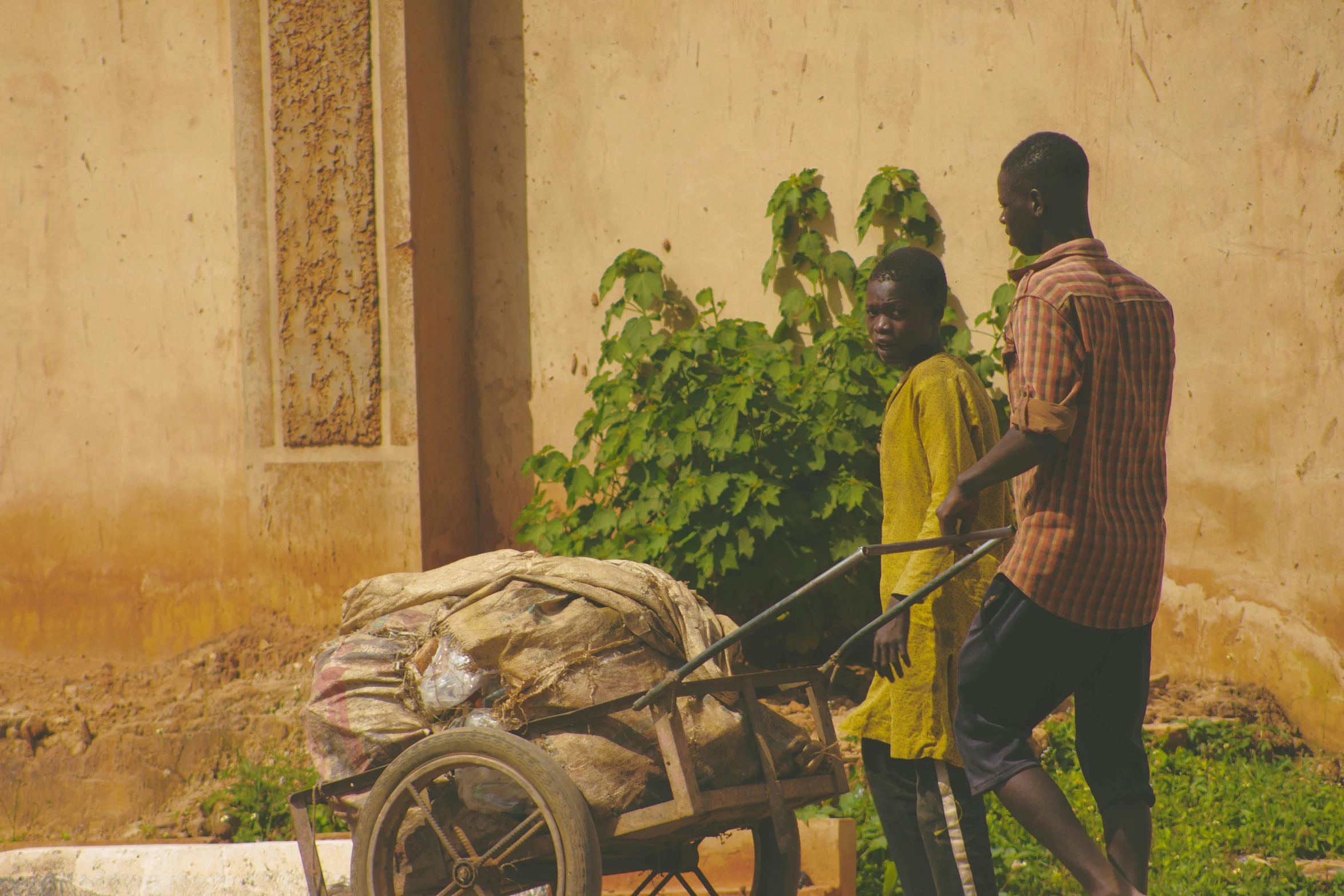 two men walking next to a cart filled with potatoes