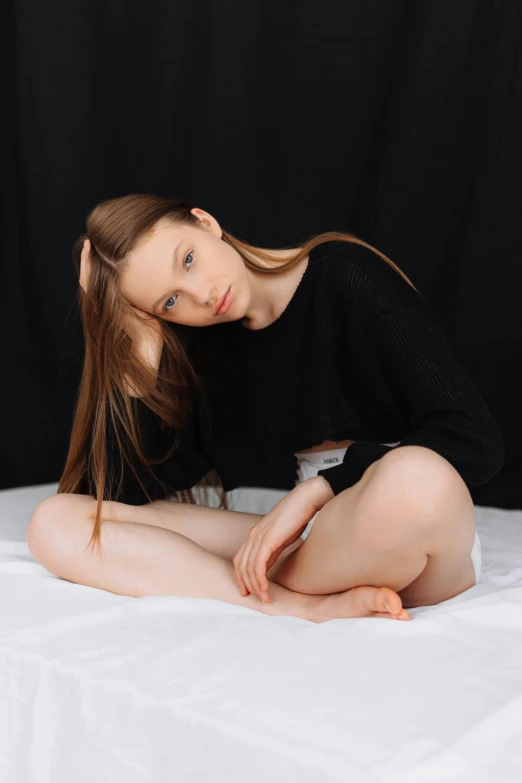 a young woman posing in black sitting on a white bed