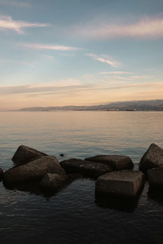 some rocks in water and a hill in the background