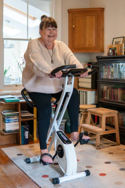 the woman smiles while riding her exercise bike in the living room