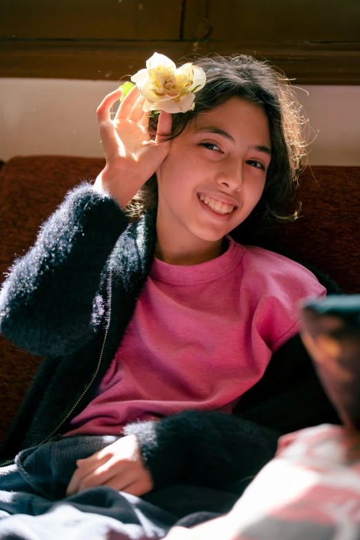 a girl sitting down and holding up a flower