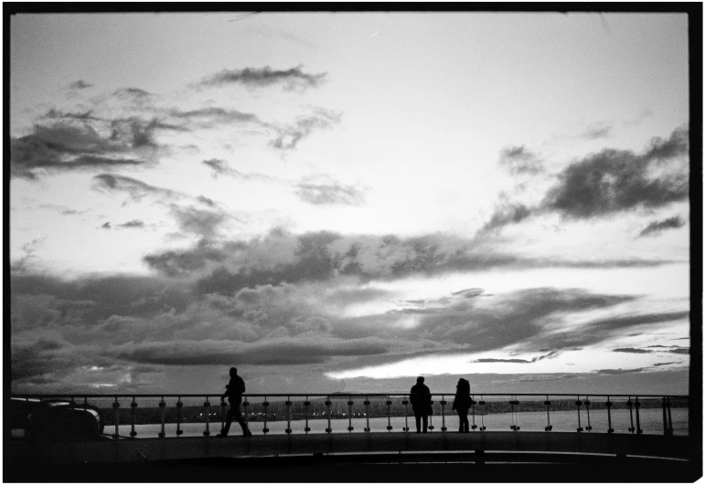 two people on a dock with the sky and clouds