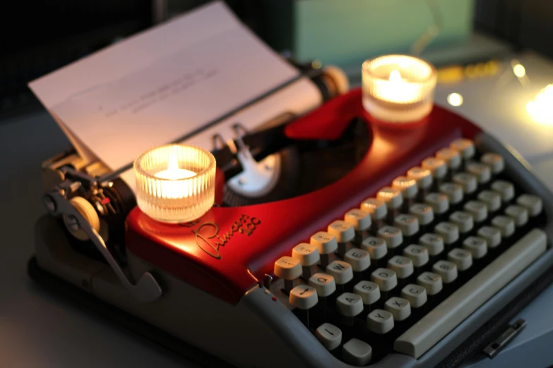 an old - fashioned typewriter has two lit candles in front of it