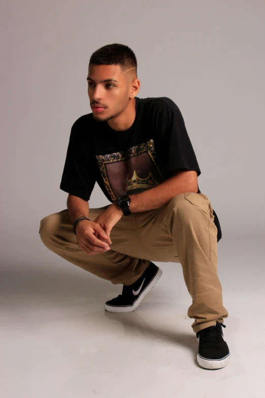 a man crouching on the ground, in a black shirt and khaki pants