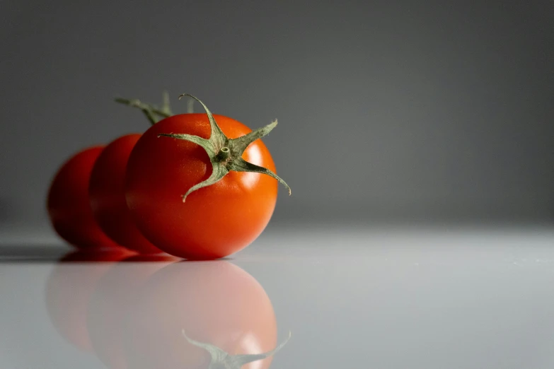 two tomatoes are one in the foreground while the other in the background on the ground