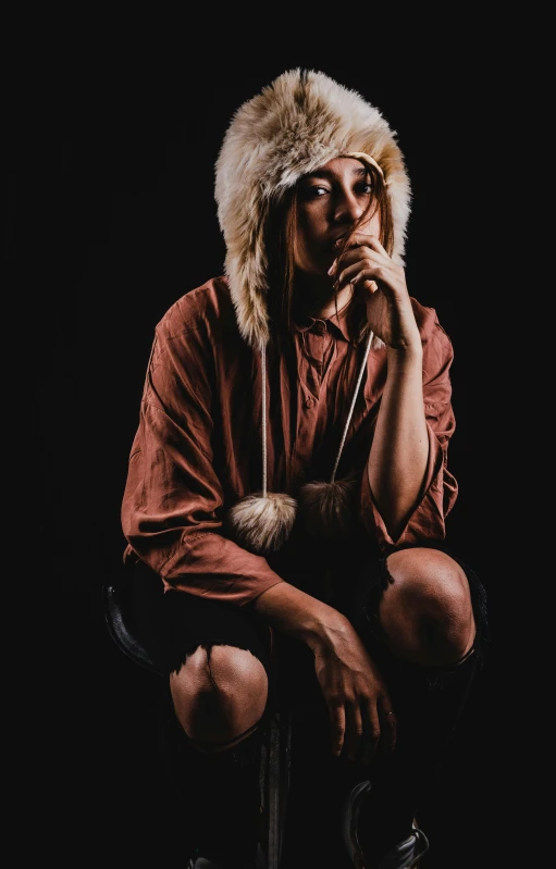 a woman sitting on a chair while wearing a fur hat