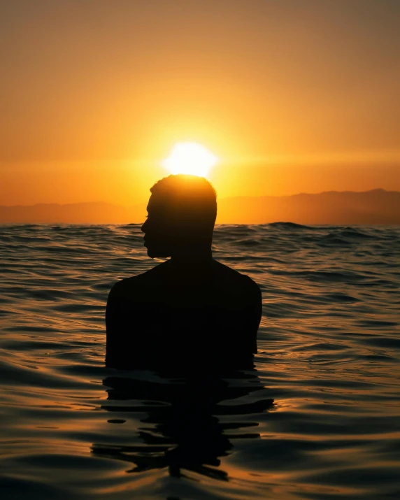 the sun rising as the silhouette of a person in the water