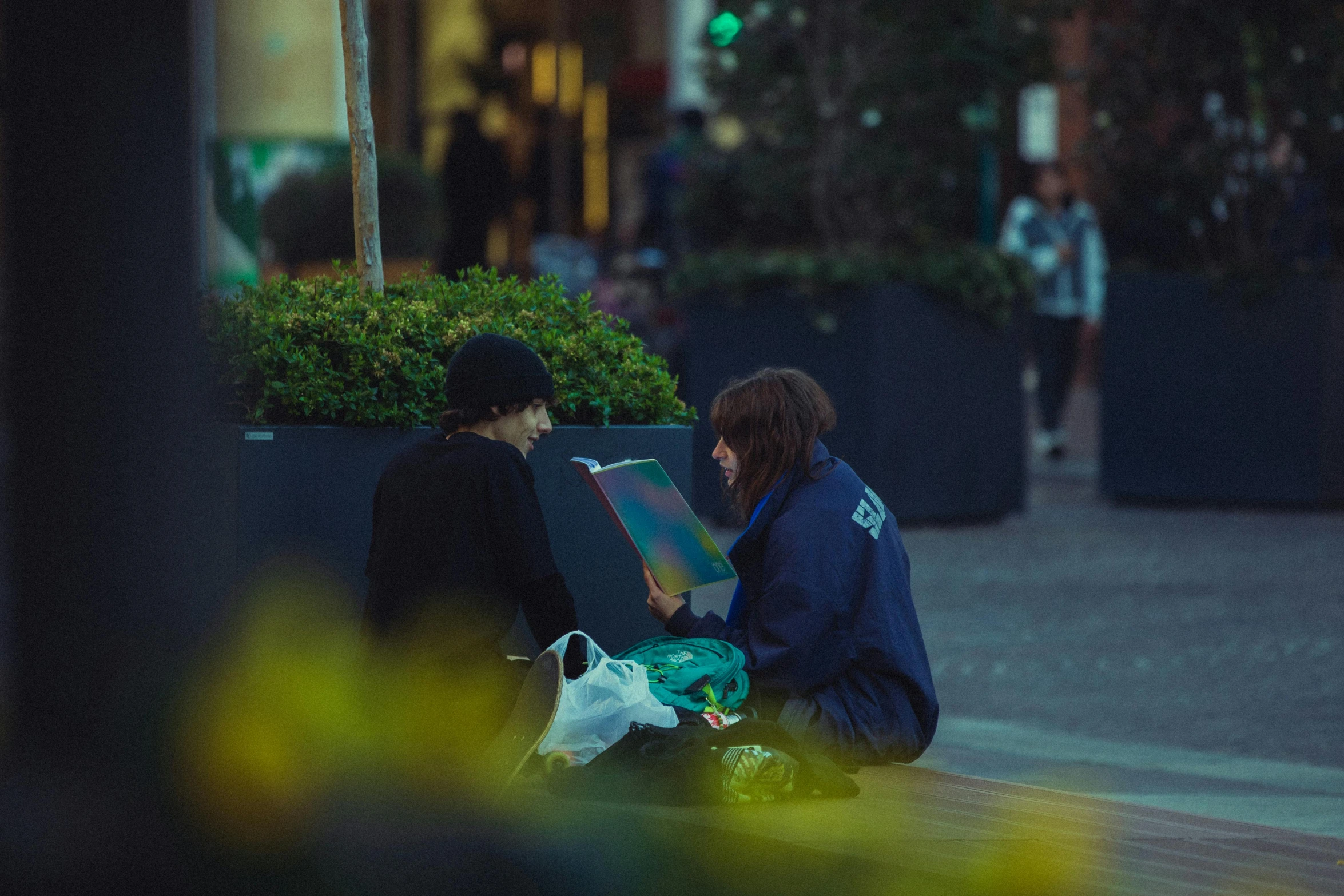 two women sitting on the ground, one has a painting on the table