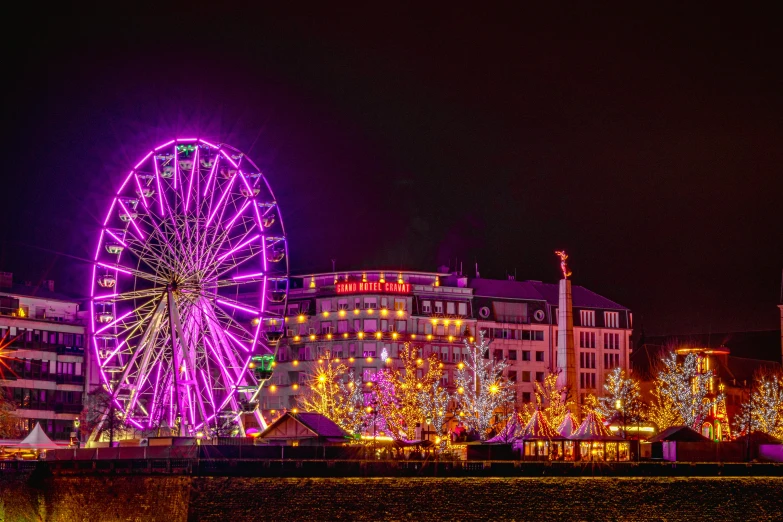 a ferris wheel sits on the side of a river in the night