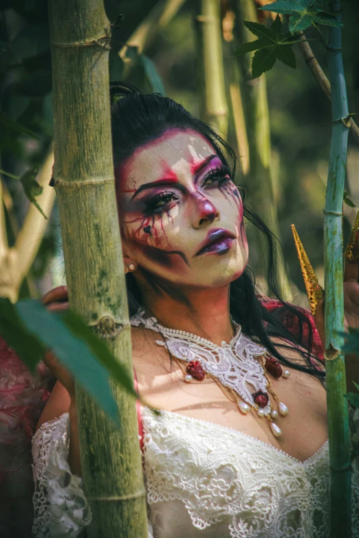 the woman with face paint looks over a bamboo tree