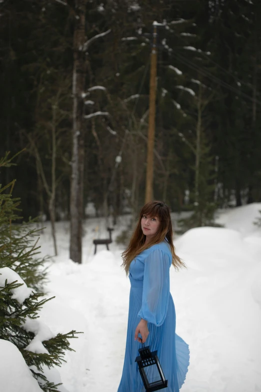 a young lady wearing a blue dress holds an item in the snow