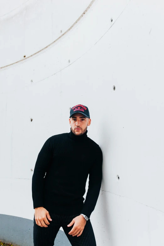 a man leaning against a wall with a black outfit