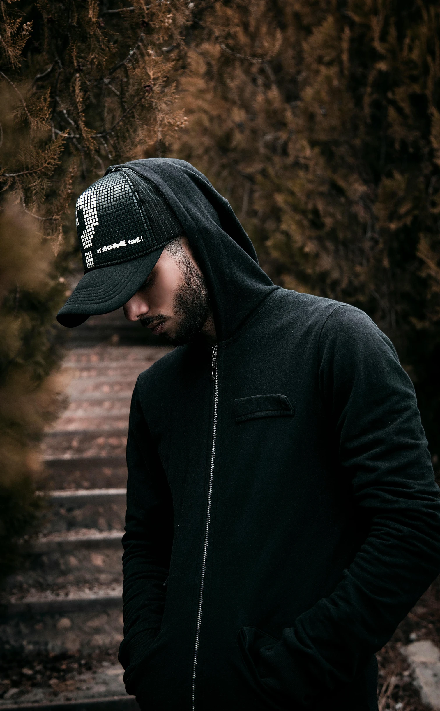 man with black jacket and hood in the middle of a wooded area