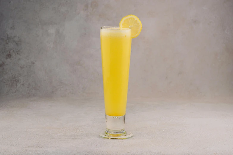 a tall glass with yellow liquid and a half lemon on it
