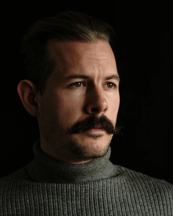 a man with a mustache and sweater looking straight ahead