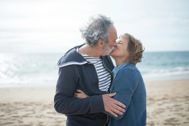 a woman kisses her man's forehead at the beach