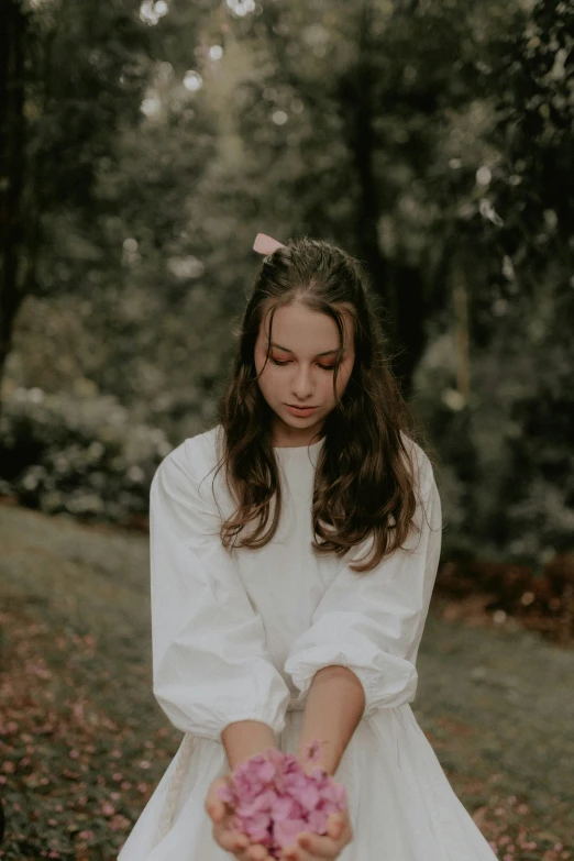 the girl is wearing a dress that is white and holding a pink flower