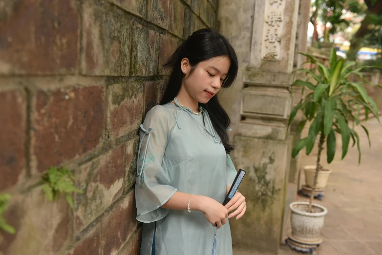 a woman is leaning against a wall holding her cell phone