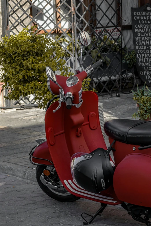 a red scooter parked on a sidewalk with plants