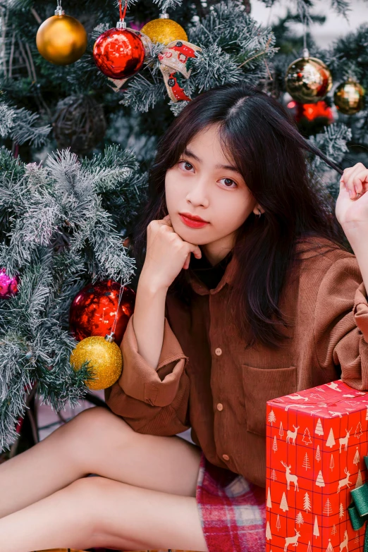 an asian woman wearing a christmas hat sitting by a tree
