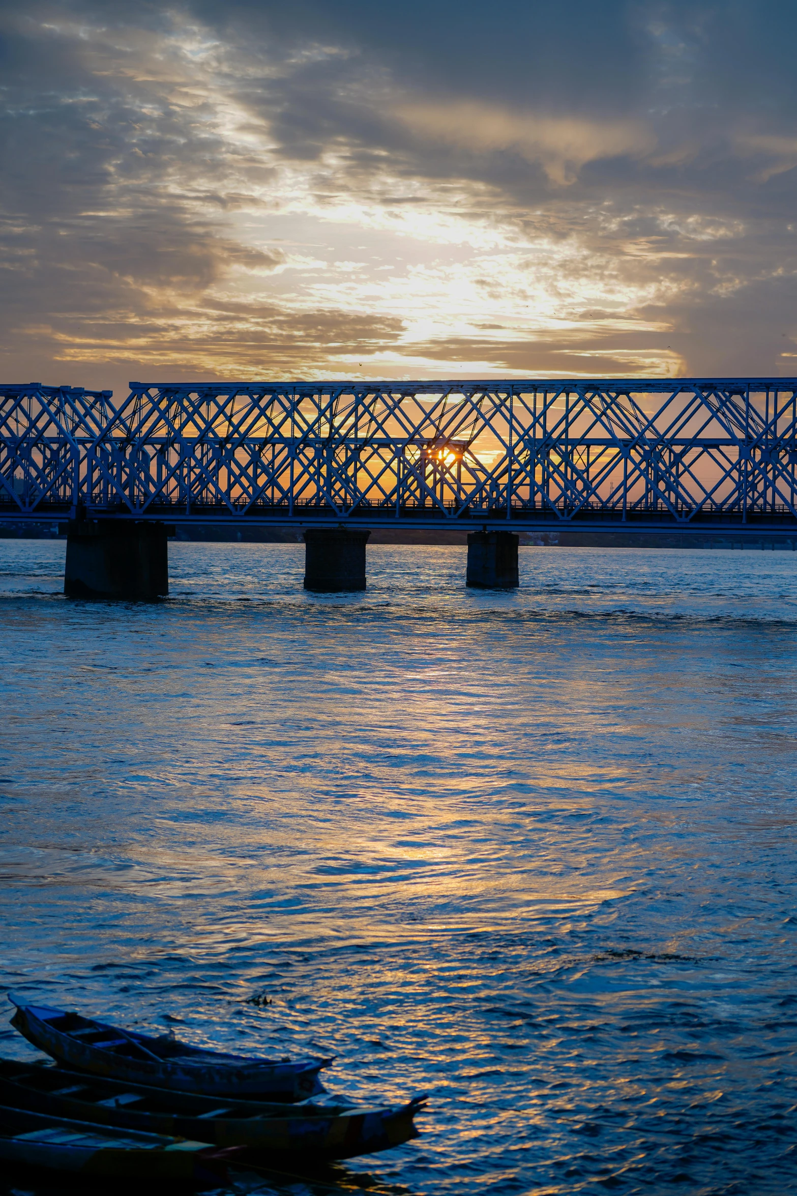 a bridge over some water with a sun peeking through the clouds