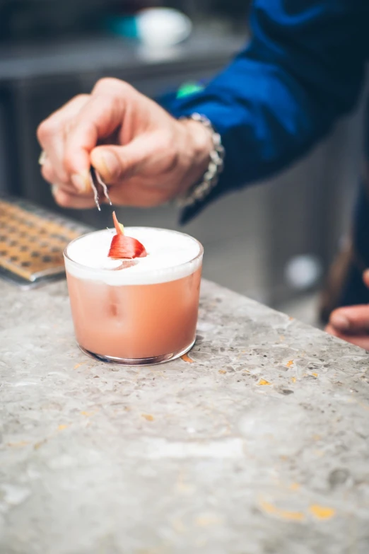 a hand dipping a small piece of fruit on top of a drink