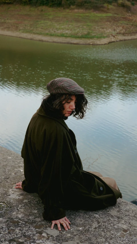 a person with his head down sitting on a rock near the water