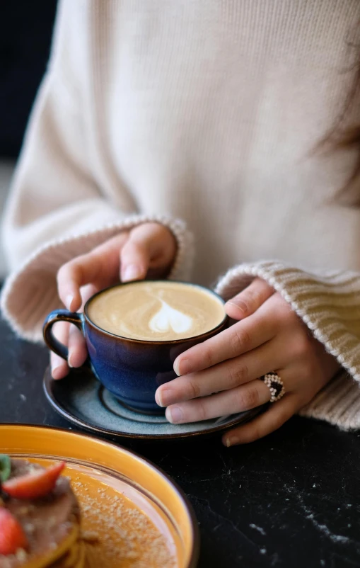 woman in sweater holding a cup with pastry on top