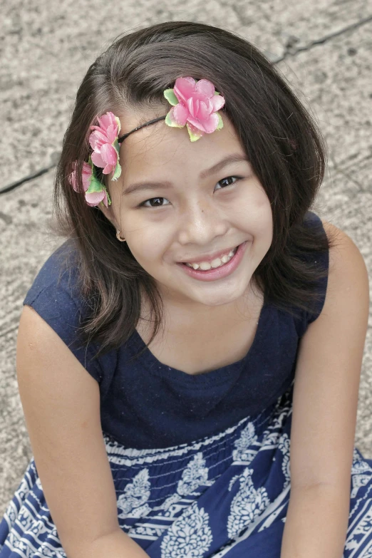 a smiling girl sitting on the ground with pink flowers in her hair