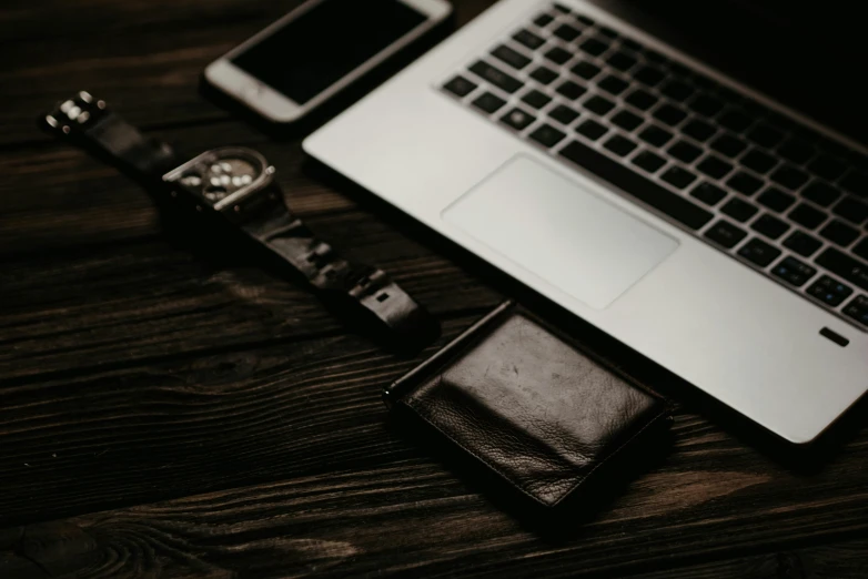 a wallet sitting next to a wrist watch and a laptop