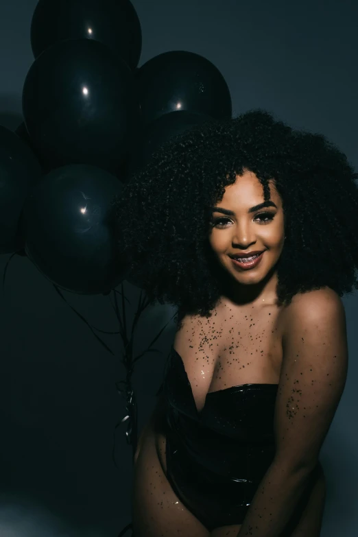 a young woman is standing with her arm on the back of her chest holding two black balloons