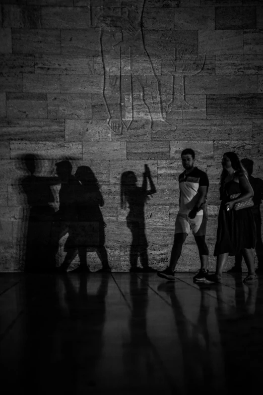 people stand next to a brick wall with a wall that has text projected onto it