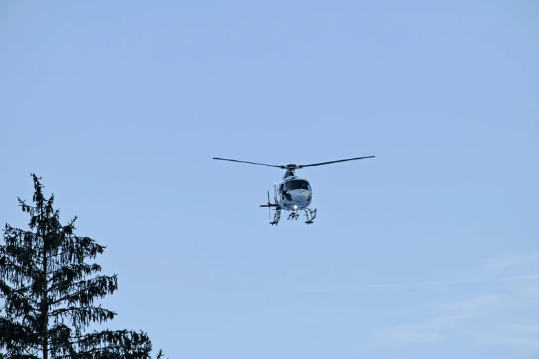 the large helicopter is flying overhead by a tree