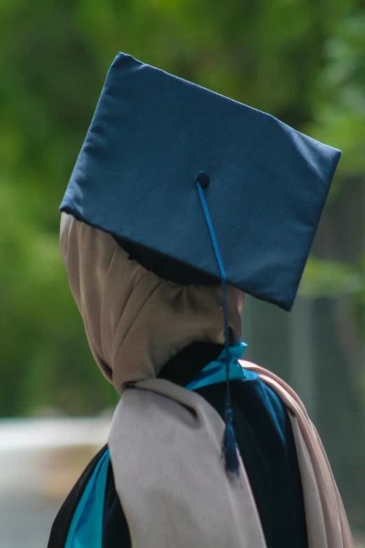 a person with a hood and blue graduation cap on, walking outside