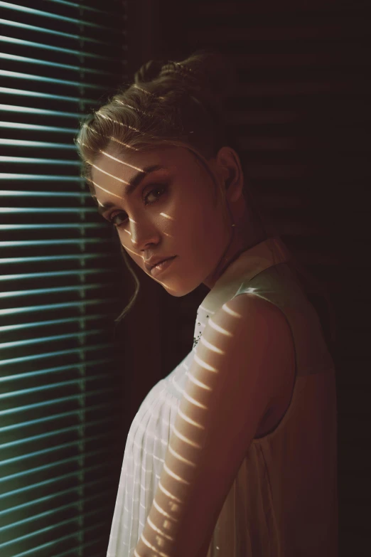 a young woman poses by a window near blinds