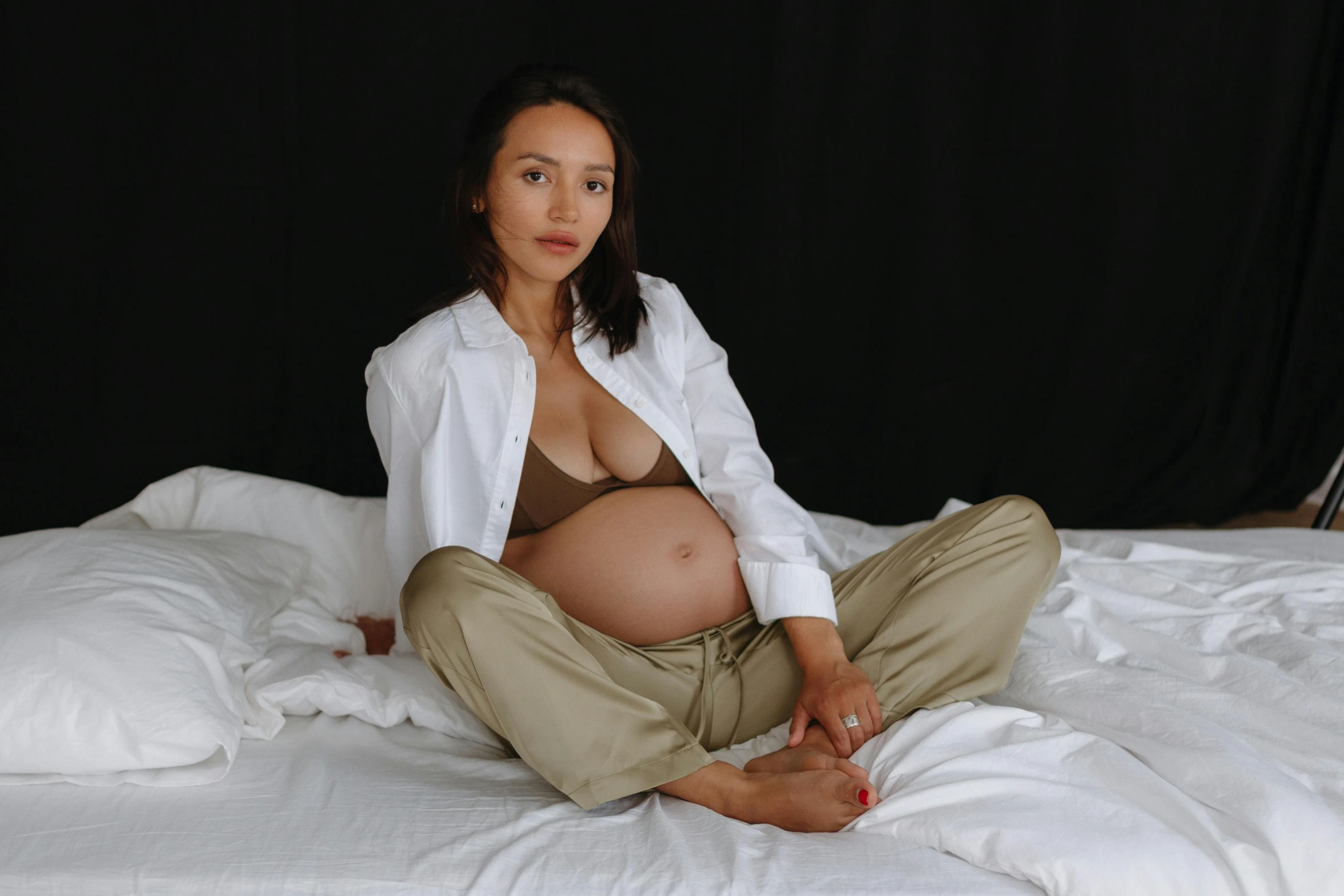 pregnant woman sitting on top of bed in tan pants