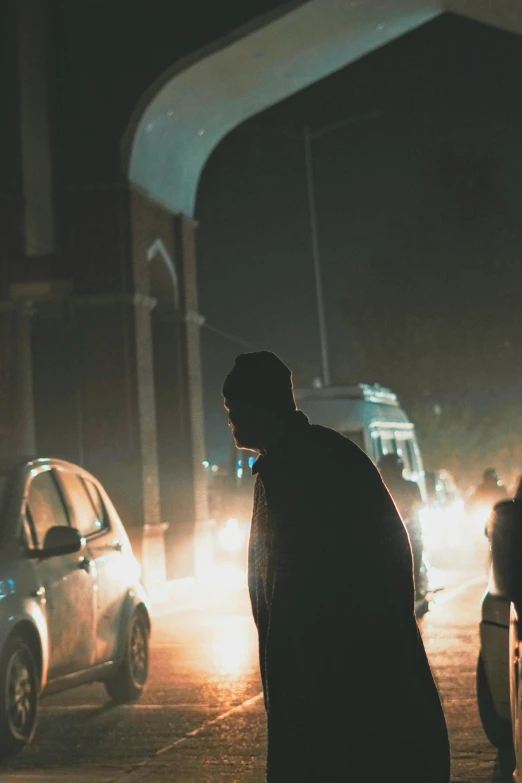 a man stands next to his car on a city street at night