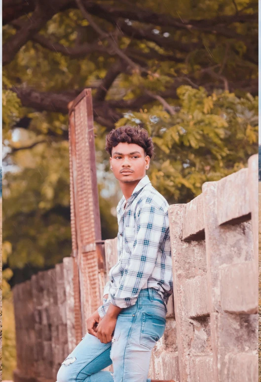 a young man wearing blue pants leaning on a wall