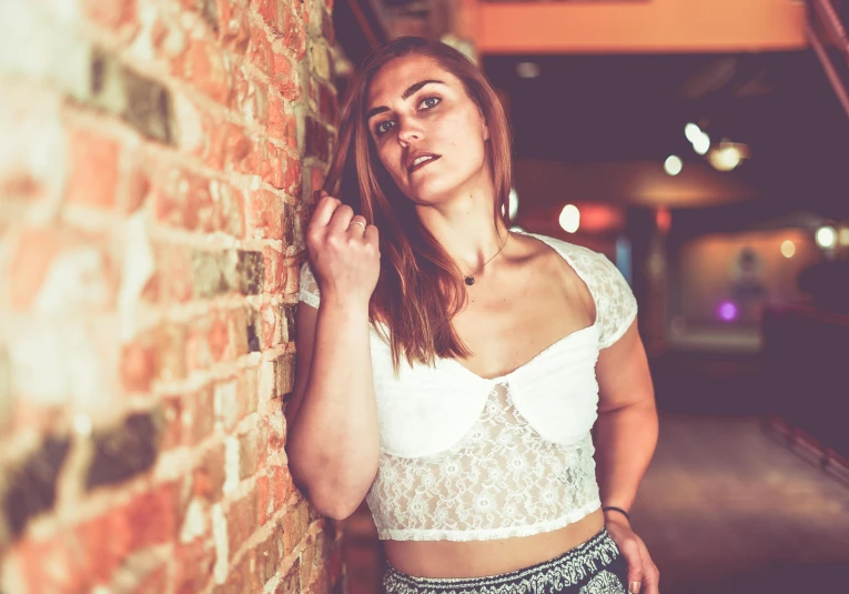 a beautiful young woman standing next to a brick wall