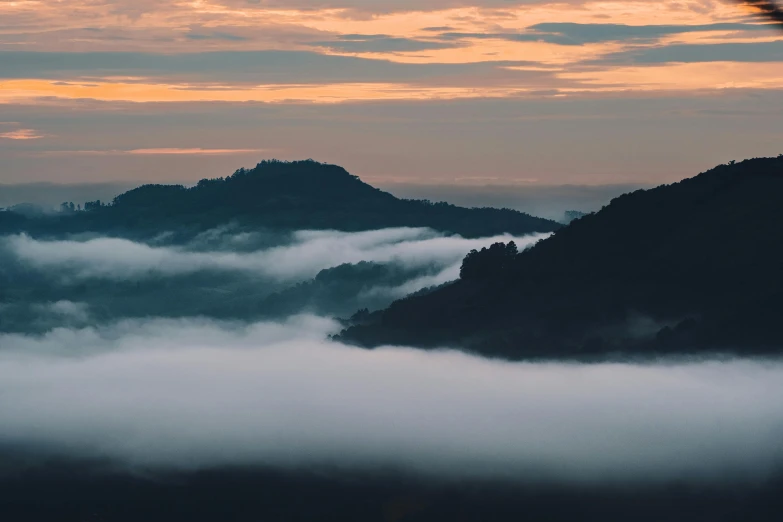 a hill with some clouds at sunrise with the sky