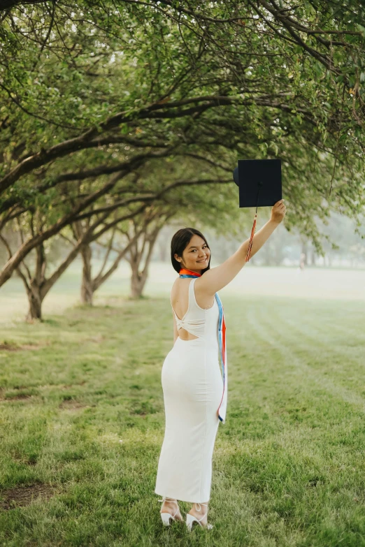 a woman holding up a hat standing on a lush green field