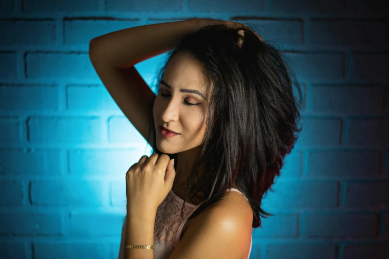 woman with hands on head in front of blue brick wall