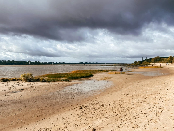 a couple riding horses on a sandy beach under cloudy skies